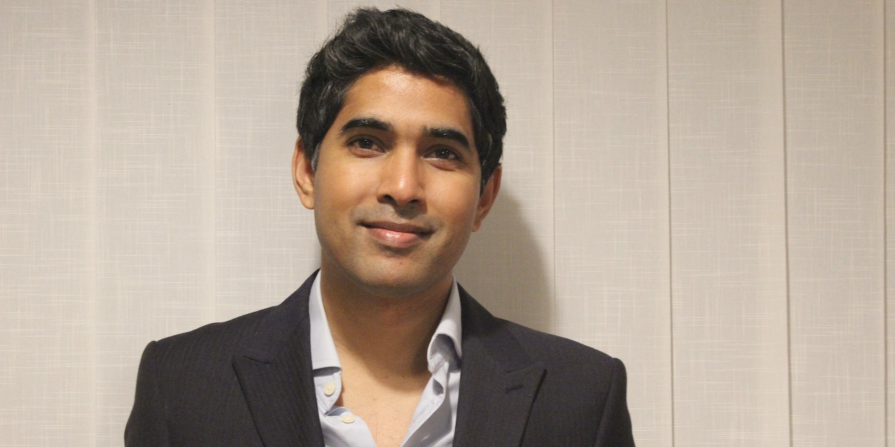 Humayon Pramanik, an Asian man, with short dark hair, smiles at the camera. He wears an open necked grey shirt and dark blazer